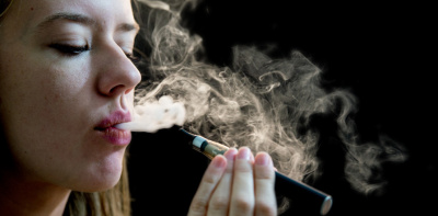 A woman using an e-cigarette. A cloud of vapour exits her mouth.