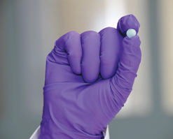 A gloved hand holding a blue pill